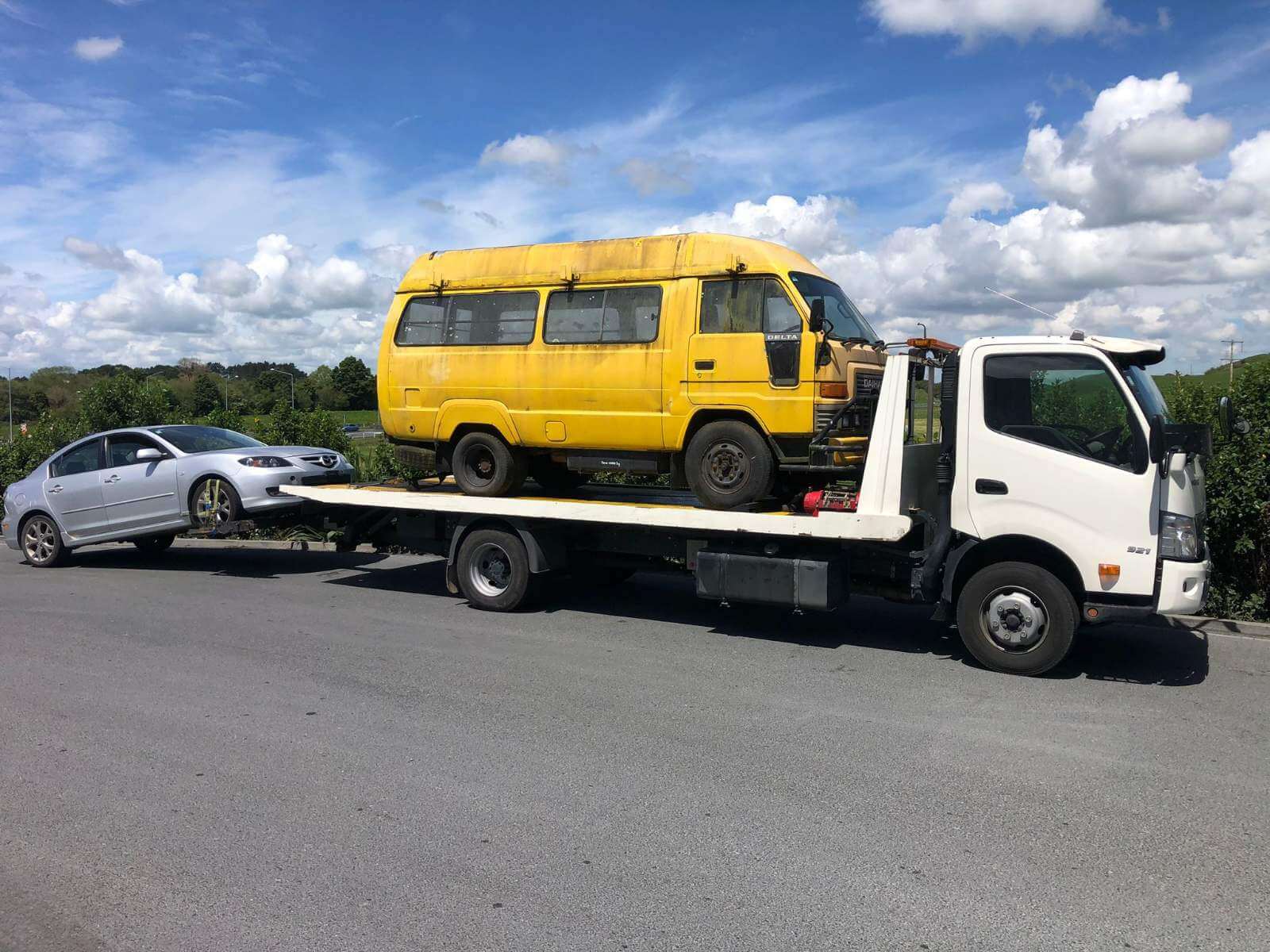 Car removals tow truck carrying a yellow van and towing a silver car in Whangarei